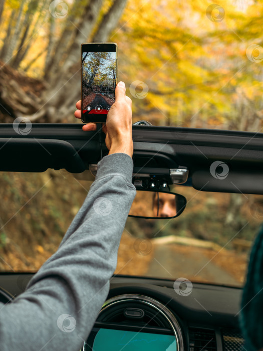Скачать Мужчина снимает вертикальное видео на мобильный телефон из машины на дороге в красивом осеннем лесу фотосток Ozero