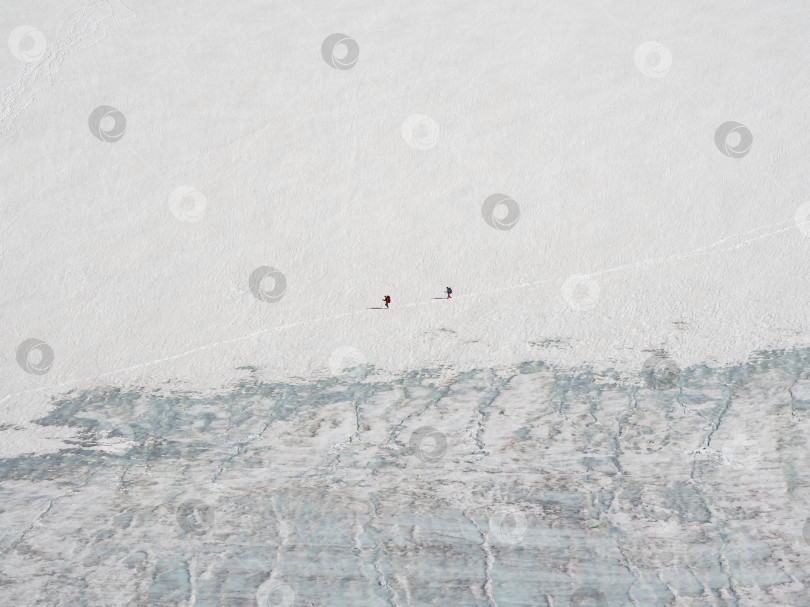 Скачать Минималистичный пейзаж с двумя маленькими туристами на леднике. Экстремальный отдых и горный туризм. Команда туристов поднимается по горной тропе. фотосток Ozero