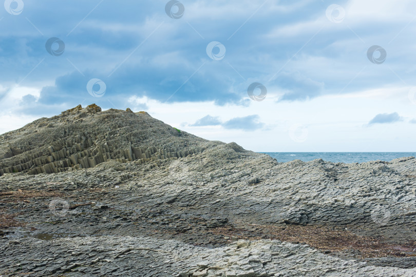 Скачать скалистый берег моря из столбчатого гранита, застывшей лавы, напоминающей чешую или булыжную мостовую, побережье острова Кунашир фотосток Ozero
