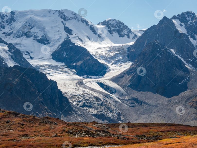 Скачать Живописный горный пейзаж с большим извилистым ледником на скалистом холме. Потрясающий пейзаж с каменистым перевалом, покрытым снегом в солнечном свете. фотосток Ozero