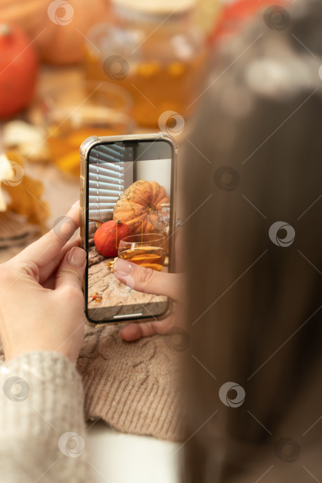 Скачать Девушка фотографирует тыквы, осенние листья и чайник на окне. Девушка фотографирует на телефон деревенскую композицию на Хэллоуин. Счастливого Дня благодарения и Хэллоуина фотосток Ozero