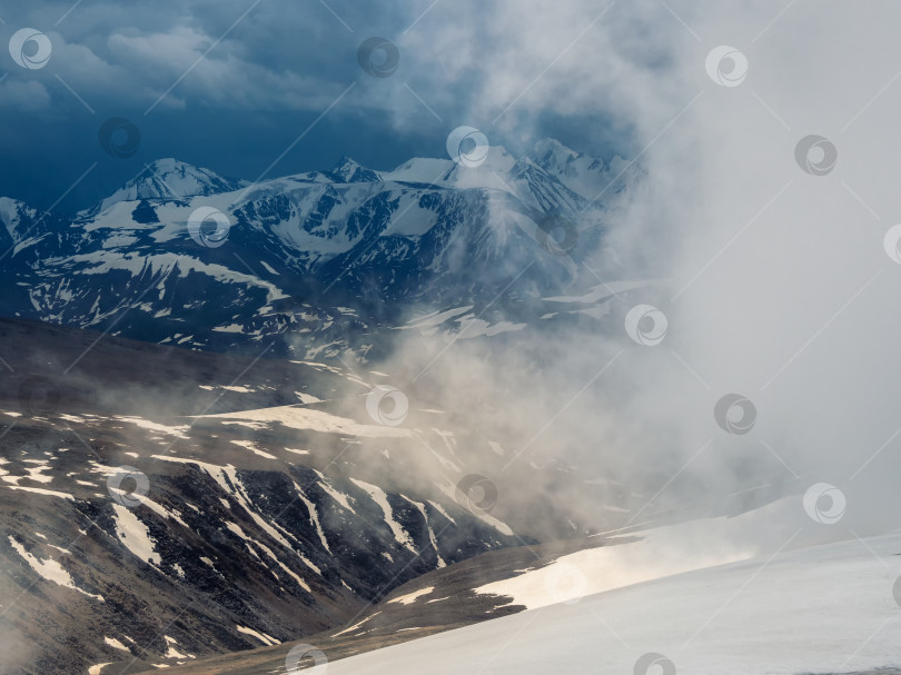 Скачать Шторм на вершине горы. Чудесный драматический пейзаж с большими заснеженными горными вершинами над низкими облаками. Атмосферные большие снежные горные вершины в облачном небе. фотосток Ozero