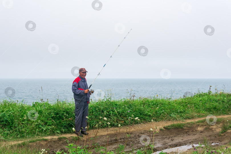 Скачать мужчина-рыбак проверяет свою удочку на берегу моря фотосток Ozero