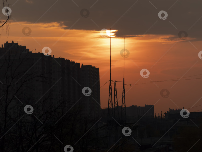 Скачать Закат в большом городе между зданиями и опорами электропередачи в тени на фоне большого солнца фотосток Ozero