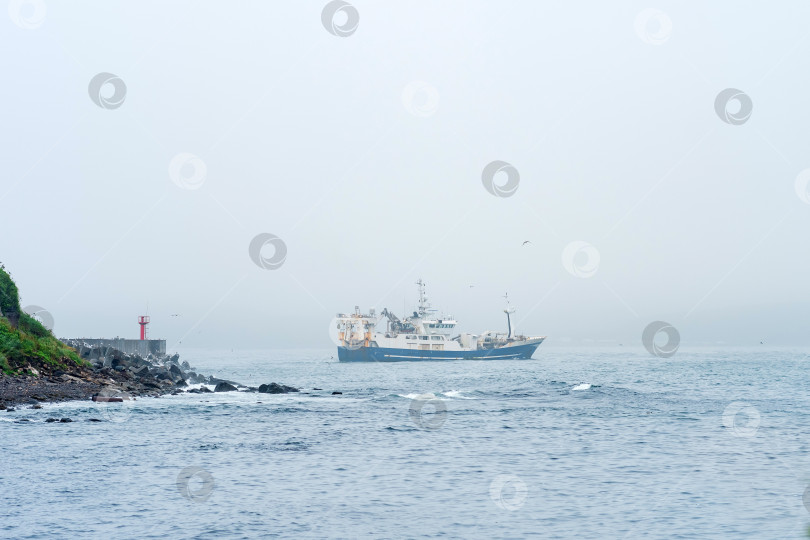 Скачать рыболовецкое судно выходит из-за мыса с маяком, плывя в туманное море фотосток Ozero
