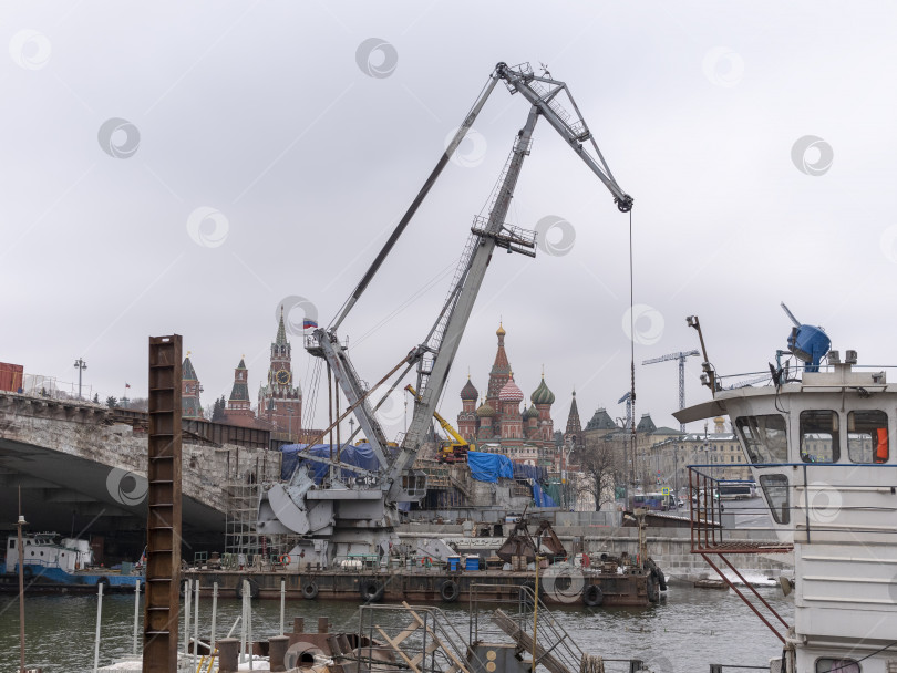 Скачать МОСКВА, РОССИЯ - 01 мая 2021 года: строительный кран с удлиненной стрелой возле Большого каменного моста через Москву-реку, на фоне Кремлевского холма фотосток Ozero