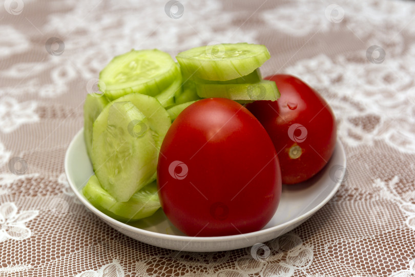 Скачать Свежие помидоры с огурцами на белой тарелке на столе, покрытом скатертью фотосток Ozero