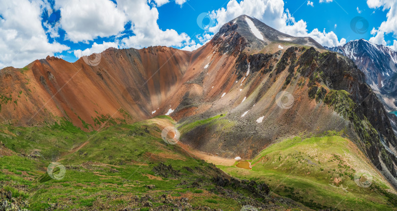 Скачать Летний пейзаж с высокогорной долиной среди заснеженного горного хребта и остроконечной вершиной под облачным голубым небом. Атмосферный горный пейзаж с тенистой зеленой долиной среди скалистых гор. фотосток Ozero