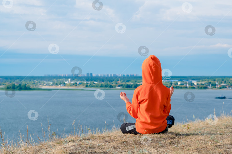 Скачать мальчик медитирует на склоне холма на фоне моря. Красивый морской пейзаж с медитирующим мальчиком сзади. Психическое здоровье с детства. Гармония с природой. Место для медитации на холме. фотосток Ozero