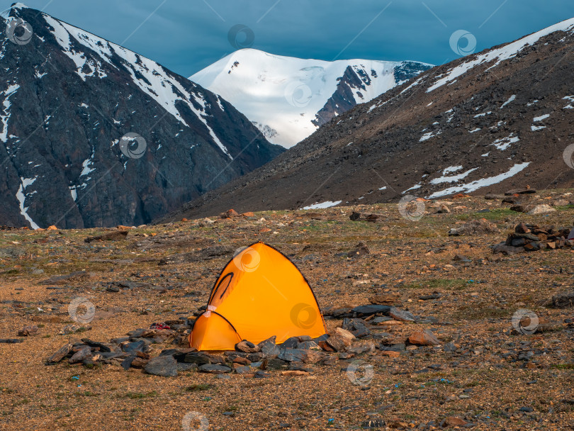 Скачать Одиночный поход. Разбив лагерь на скалистом высокогорном плато. Желтая палатка на фоне ледника и высоких заснеженных гор. фотосток Ozero