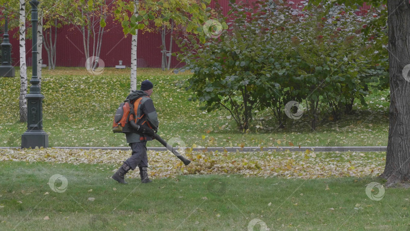Скачать Рабочий обдувает осенние листья вакуумной воздуходувкой фотосток Ozero