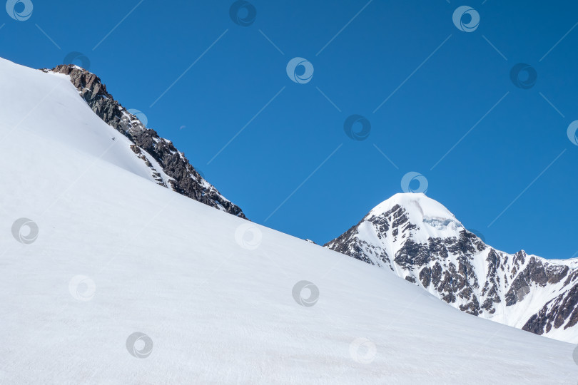 Скачать Снежные заносы на горном склоне. Атмосферный горный пейзаж с ледником на скалистом холме. Потрясающий пейзаж с каменистым перевалом, покрытым снегом в солнечном свете. фотосток Ozero