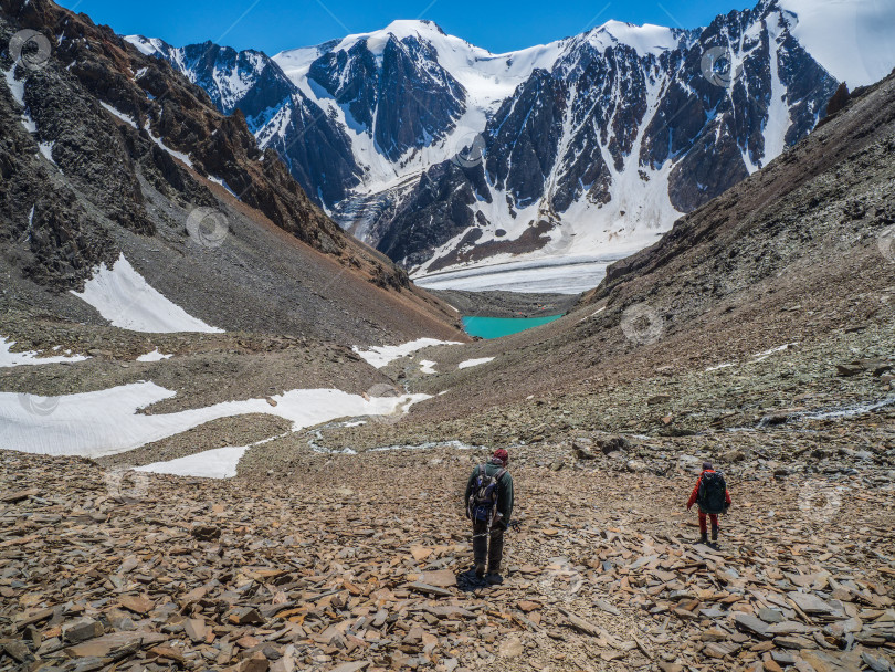 Скачать Уставшие альпинисты спускаются по крутому горному склону с россыпью камней. Группа туристов в горах. Стиль жизни в путешествиях, пешие походы по сложным трассам, концепция приключений на летних каникулах. фотосток Ozero