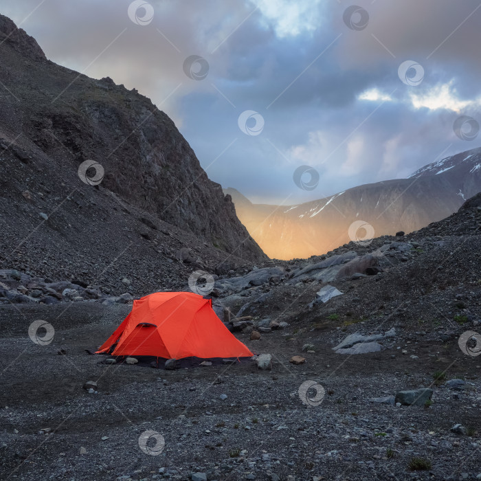 Скачать Квадратный вид на сюрреалистический альпийский пейзаж с палаткой на скалистом холме среди скал на восходе солнца. Прекрасные утренние горы в низких облаках. Сюрреалистический пейзаж с палаткой в высокогорье в пасмурную погоду. фотосток Ozero