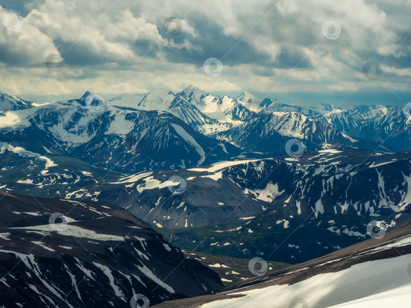 Скачать Пестрый потрясающий вид с высоты птичьего полета на снежные горы под облачным небом. Живописный горный пейзаж на большой высоте с облачностью. Атмосферный горный фон с красивым заснеженным горным хребтом. фотосток Ozero