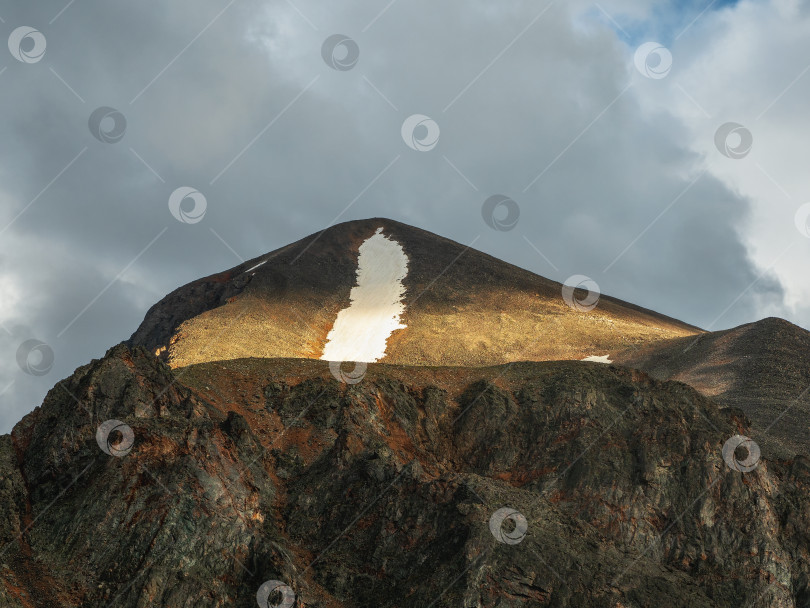 Скачать Кальдера залита солнечным светом. Пейзаж с залитым солнцем широким острым горным хребтом между горными вершинами. Красочный горный пейзаж с большими острыми скалами на вершине хребта в солнечном свете под облачным небом. фотосток Ozero