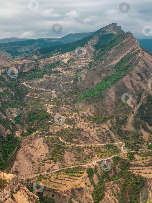 Скачать Вертикальный вид на горную долину с извилистой дорогой. Опасная узкая грунтовая горная дорога через холмы к высокогорной деревне. фотосток Ozero