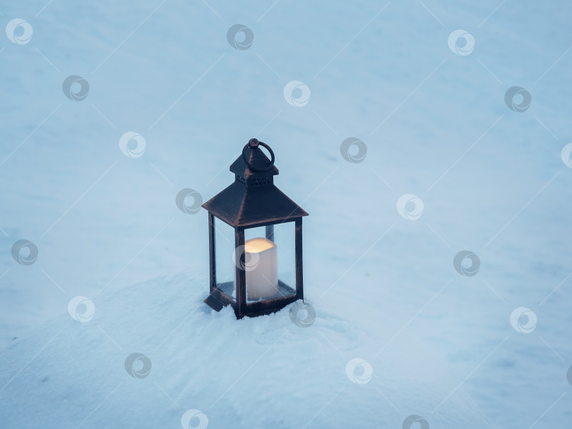 Скачать Старый фонарь со свечой стоит на вечернем снегу морозной зимой. фотосток Ozero