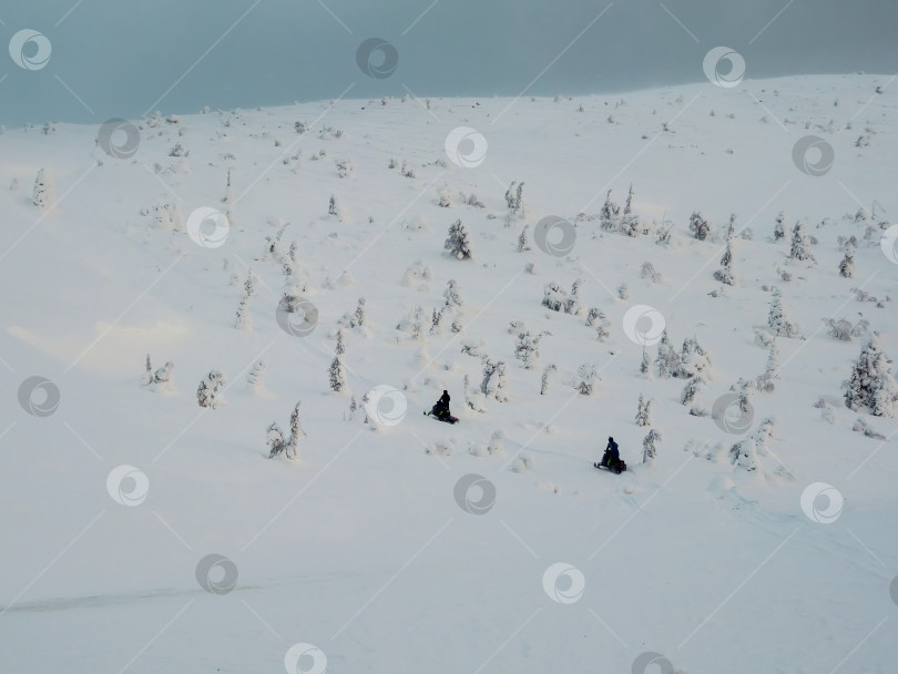 Скачать Снегоходы на полярной горке. Два человека поднимаются на холм на снегоходах. фотосток Ozero