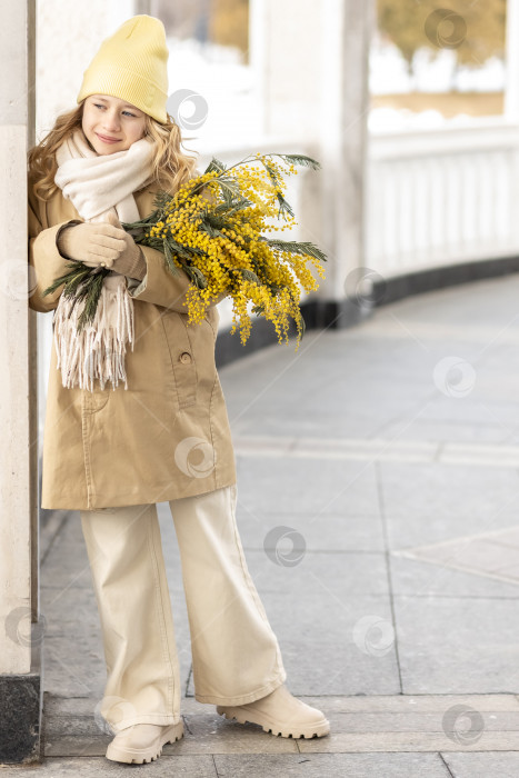 Скачать Портрет девушки в бежевом пальто с букетом мимозы в руках в парке. Весна, Международный женский день 8 марта. фотосток Ozero