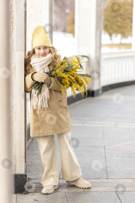 Скачать Портрет девушки в бежевом пальто с букетом мимозы в руках в парке. Весна, Международный женский день 8 марта. фотосток Ozero