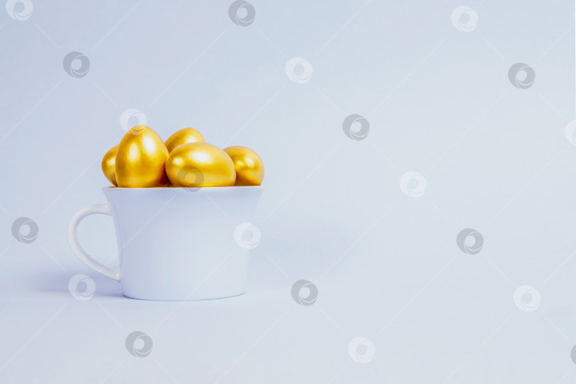 Скачать Декоративные пасхальные яйца выкрашены в золотой цвет и уложены в голубую фарфоровую чашку фотосток Ozero