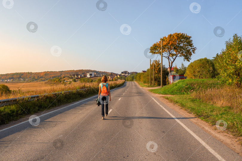 Скачать Вид сзади на женщину с рюкзаком, идущую по осенней проселочной дороге, пеший поход. фотосток Ozero