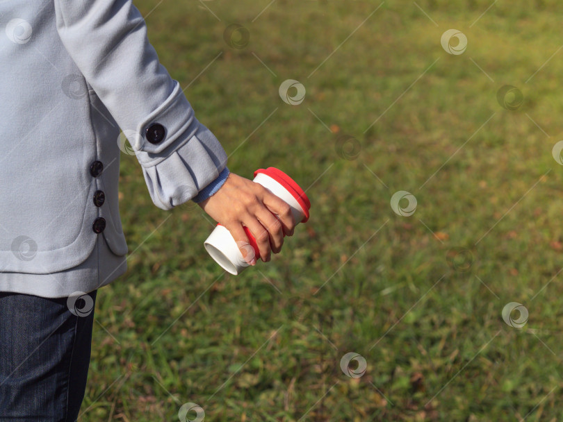 Скачать Многоразовая кофейная чашка в руках на фоне зеленой лужайки. фотосток Ozero