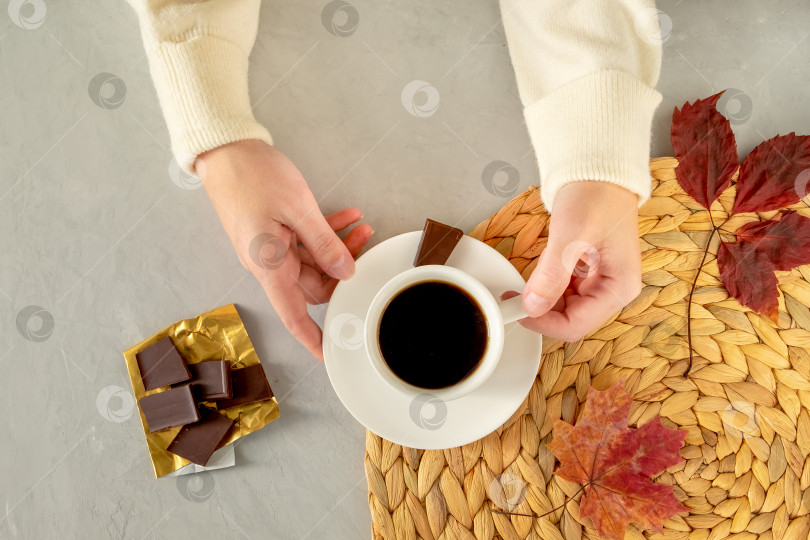 Крупным планом женские руки держат чашку кофе. Кусочки шоколада и осенние  листья на плетеной салфетке. - Ozero - российский фотосток