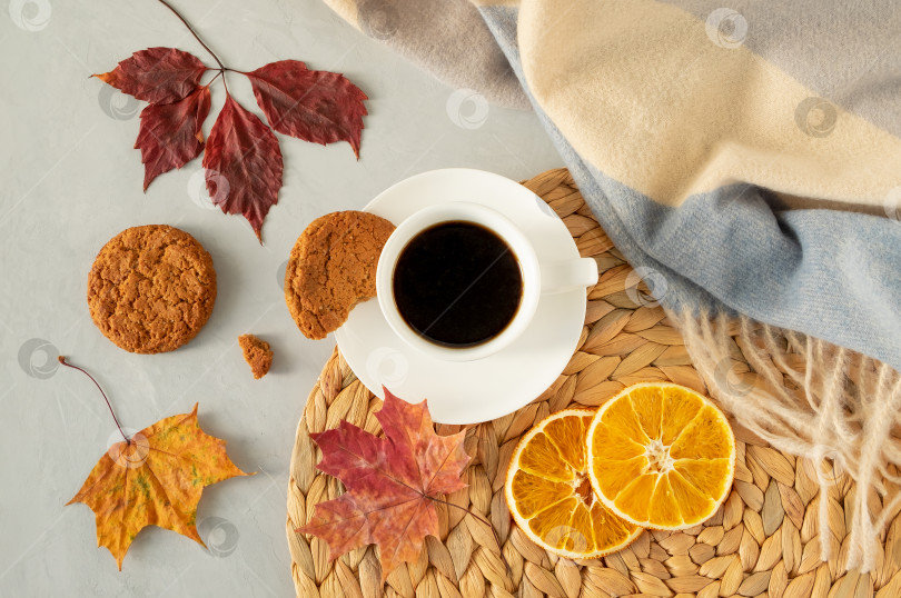 Скачать Чашка черного кофе на сером фоне с осенними листьями, теплая накидка, плетеная салфетка, овсяное печенье и ломтики сушеных апельсинов. фотосток Ozero