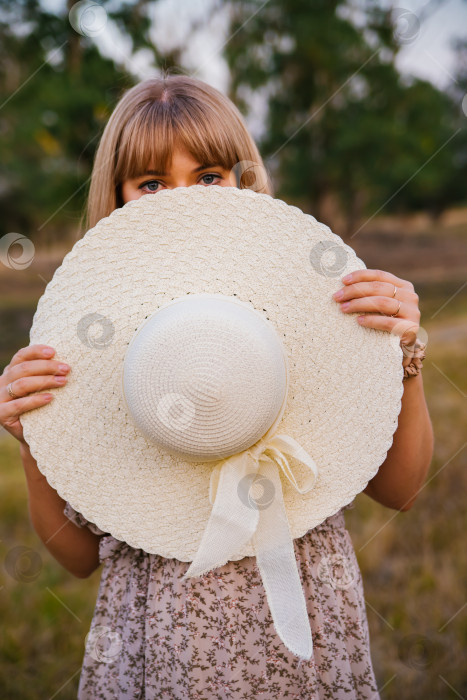 Скачать Молодая женщина закрыла лицо шляпой. Красивые глаза девушки видны из-под шляпы. Соломенная летняя шляпа, модный аксессуар. Концепция летних каникул. фотосток Ozero