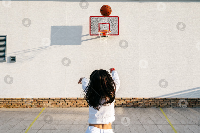 Скачать Девушка сзади бросает баскетбольный мяч в корзину на улице фотосток Ozero