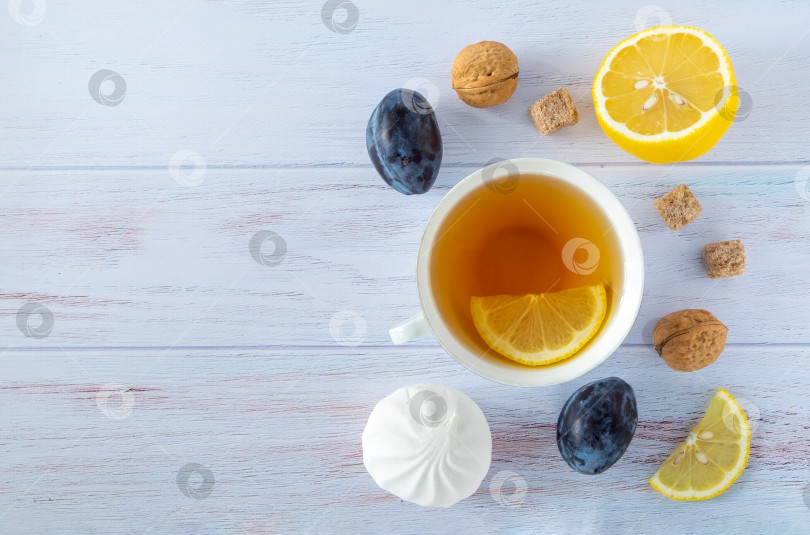 Скачать Фон для еды с белой фарфоровой чашкой чая, лимоном, спелыми сливами и нектаринами, грецкими орехами и белым зефиром на синем деревянном фоне. фотосток Ozero