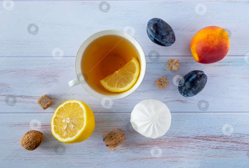 Скачать Фон для еды с белой фарфоровой чашкой чая, лимоном, спелыми сливами и нектаринами, грецкими орехами и белым зефиром. фотосток Ozero