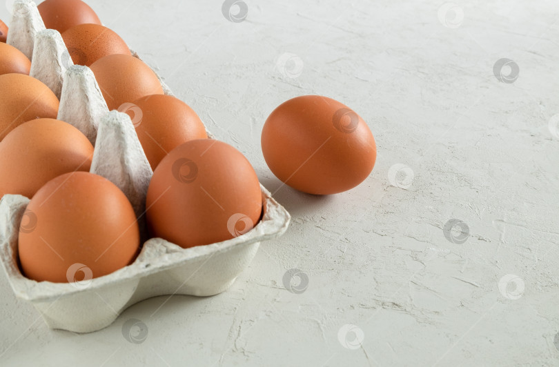 Скачать Картонный контейнер с коричневыми куриными яйцами на светло-серой штукатурной поверхности. Здоровое питание, концепция питания. фотосток Ozero