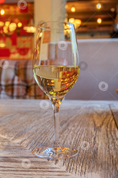 Скачать Бокал белого вина стоит на столе с деревянной поверхностью в кафе. фотосток Ozero