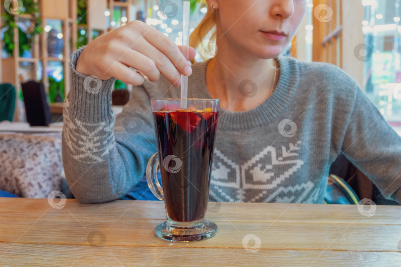 Скачать Молодая женщина в сером свитере сидит за столиком в кафе перед бокалом глинтвейна. фотосток Ozero