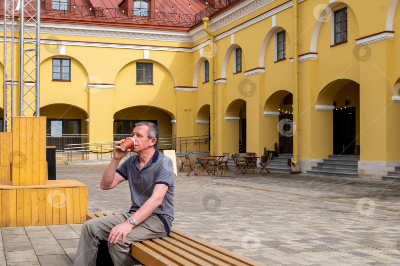 Скачать Взрослый пожилой мужчина сидит на скамейке и пьет кофе фотосток Ozero