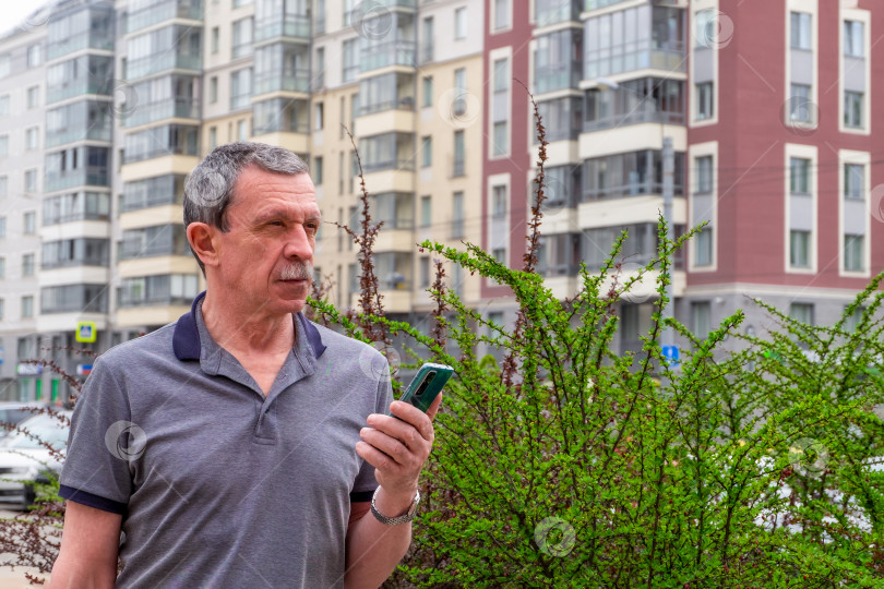Скачать Взрослый кавказский пожилой мужчина в футболке стоит на фоне жилых зданий фотосток Ozero