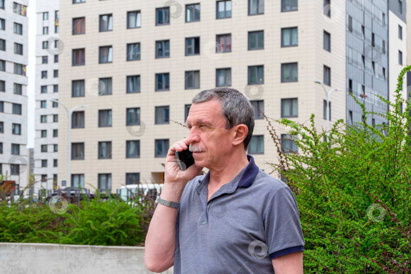 Скачать Взрослый кавказский пожилой мужчина в футболке разговаривает по смартфону фотосток Ozero