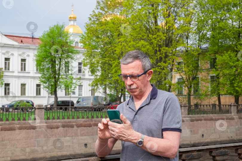 Скачать Взрослый кавказский пожилой мужчина в футболке набирает сообщение на смартфоне фотосток Ozero