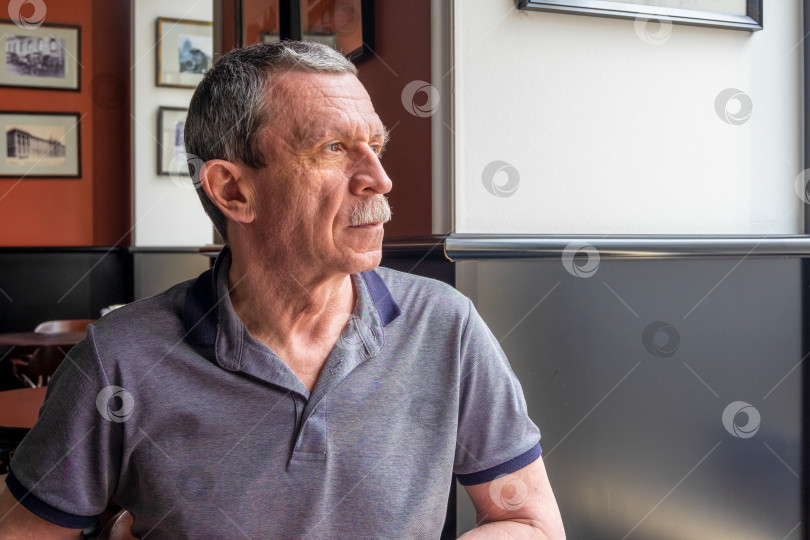 Скачать Взрослый кавказский пожилой мужчина сидит за столиком в кафе и смотрит в окно фотосток Ozero