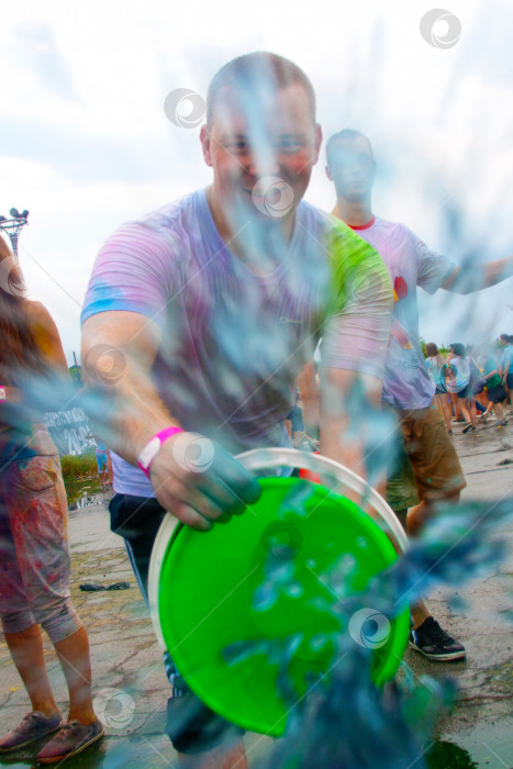 Скачать НОВОСИБИРСК, РОССИЯ - 28 июня 2014 года: Фестиваль красок. Мужчина с ведром краски выливает ее на людей. фотосток Ozero