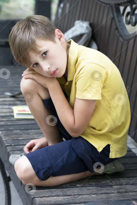Скачать Грустный маленький мальчик сидит на скамейке в парке. фотосток Ozero