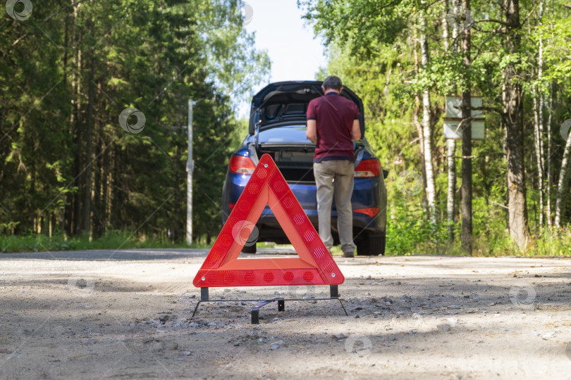 Скачать Переносной светоотражающий красный предупреждающий знак установлен на обочине дороги рядом с поврежденным транспортным средством фотосток Ozero