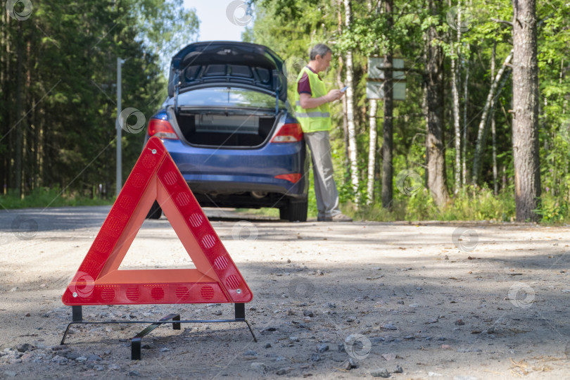 Скачать Переносной светоотражающий красный предупреждающий треугольный знак на обочине сельской дороги рядом с автомобилем фотосток Ozero