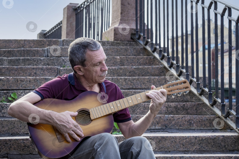 Скачать Взрослый пожилой мужчина пенсионного возраста играет на акустической гитаре на открытом воздухе фотосток Ozero