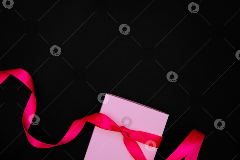 Скачать На черном фоне изображена розовая подарочная коробка. Коробка перевязана атласной лентой.Подарочная упаковка. фотосток Ozero