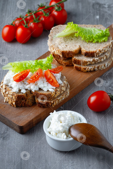 Скачать Ломтики ржаного хлеба с творогом и помидорами на деревянной тарелке на сером фоне фотосток Ozero