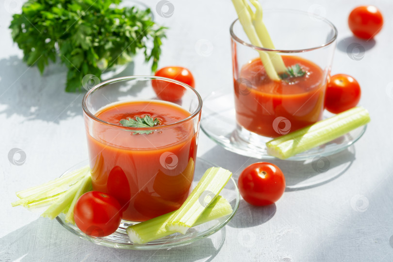 Скачать Два бокала со свежим томатным соком, сельдереем, петрушкой и спелыми помидорами на фоне светлого дерева фотосток Ozero